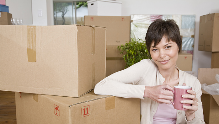 Woman with coffee sitting by moving boxes