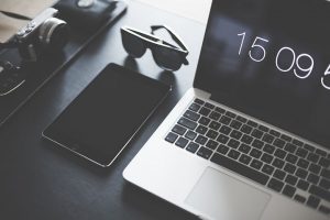 Lap top, cell phone, sunglasses on a desk